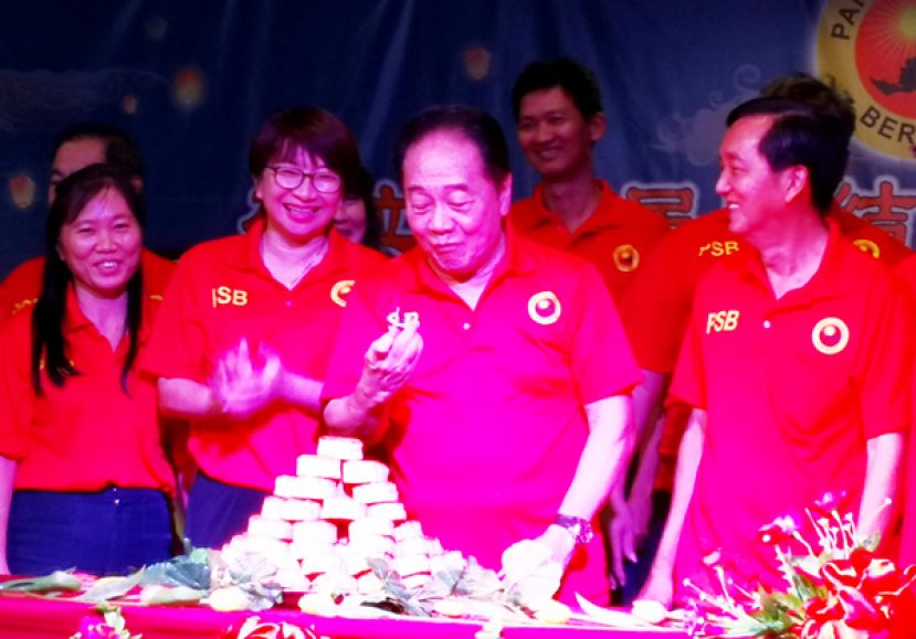  砂全民团结党主席拿督斯里黄顺舸在巴旺阿山支部中秋联欢午宴上切好月饼后，拿起月饼品尝滋味。右一;是筹备会主席甲必丹丁凤华。